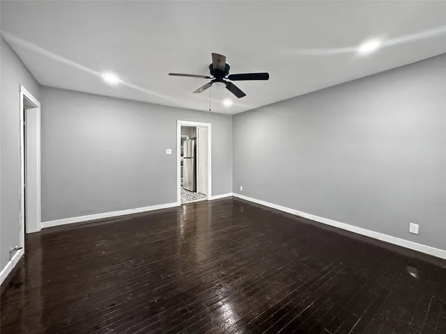 a view of an empty room with wooden floor and a ceiling fan