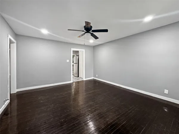 a view of an empty room with wooden floor and a ceiling fan