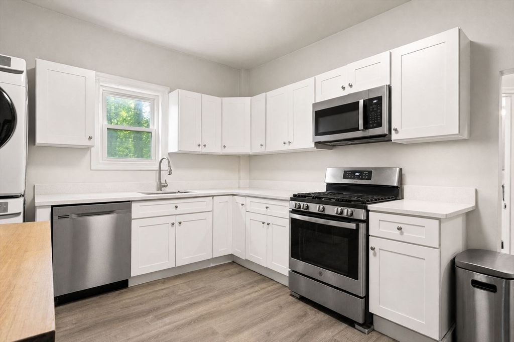 39 Union Street Boston, MA 02135 - Photo 5 of 33 a kitchen with stainless steel appliances granite countertop white cabinets a sink a stove a microwave and wooden floors