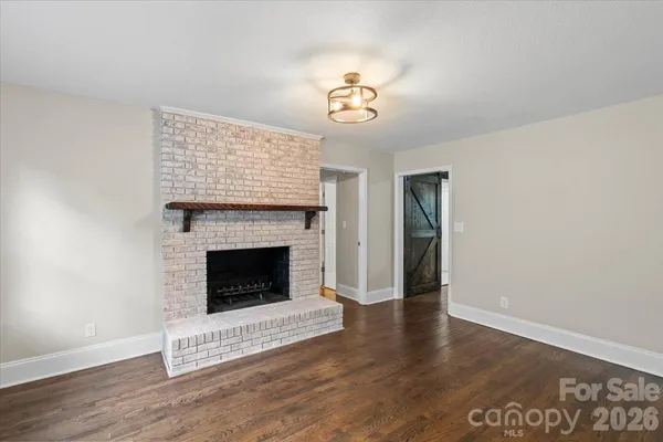 a view of an empty room with wooden floor fireplace and a window