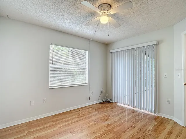 an empty room with wooden floor fan and windows