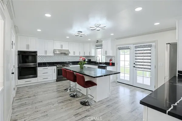 a kitchen with stainless steel appliances granite countertop a stove a sink dishwasher a refrigerator and white cabinets with wooden floor