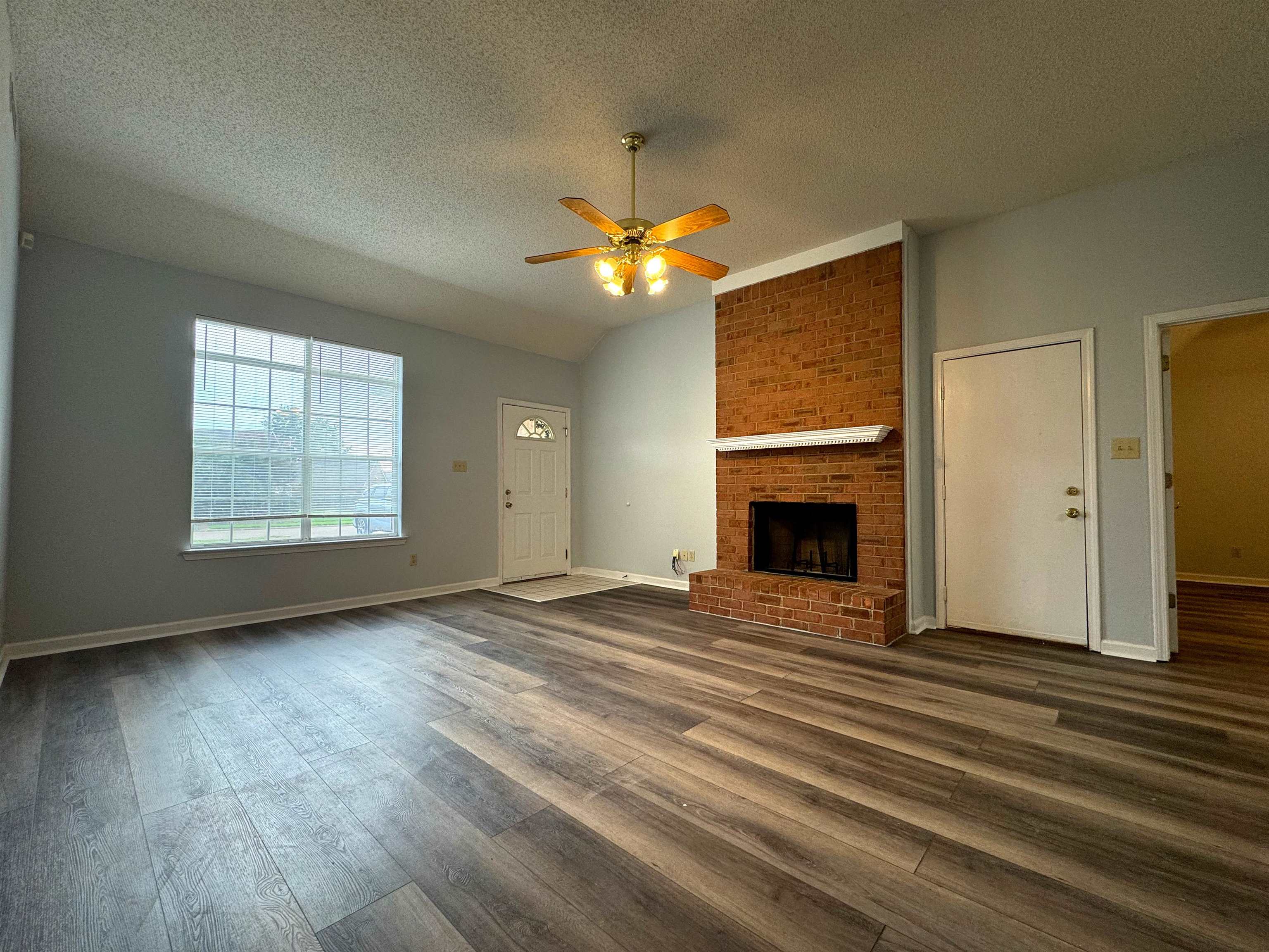 7083 Bryan Station Road Cordova, TN 38018 - Photo 4 of 19 Unfurnished living room with a textured ceiling, dark hardwood / wood-style flooring, ceiling fan, and a brick fireplace