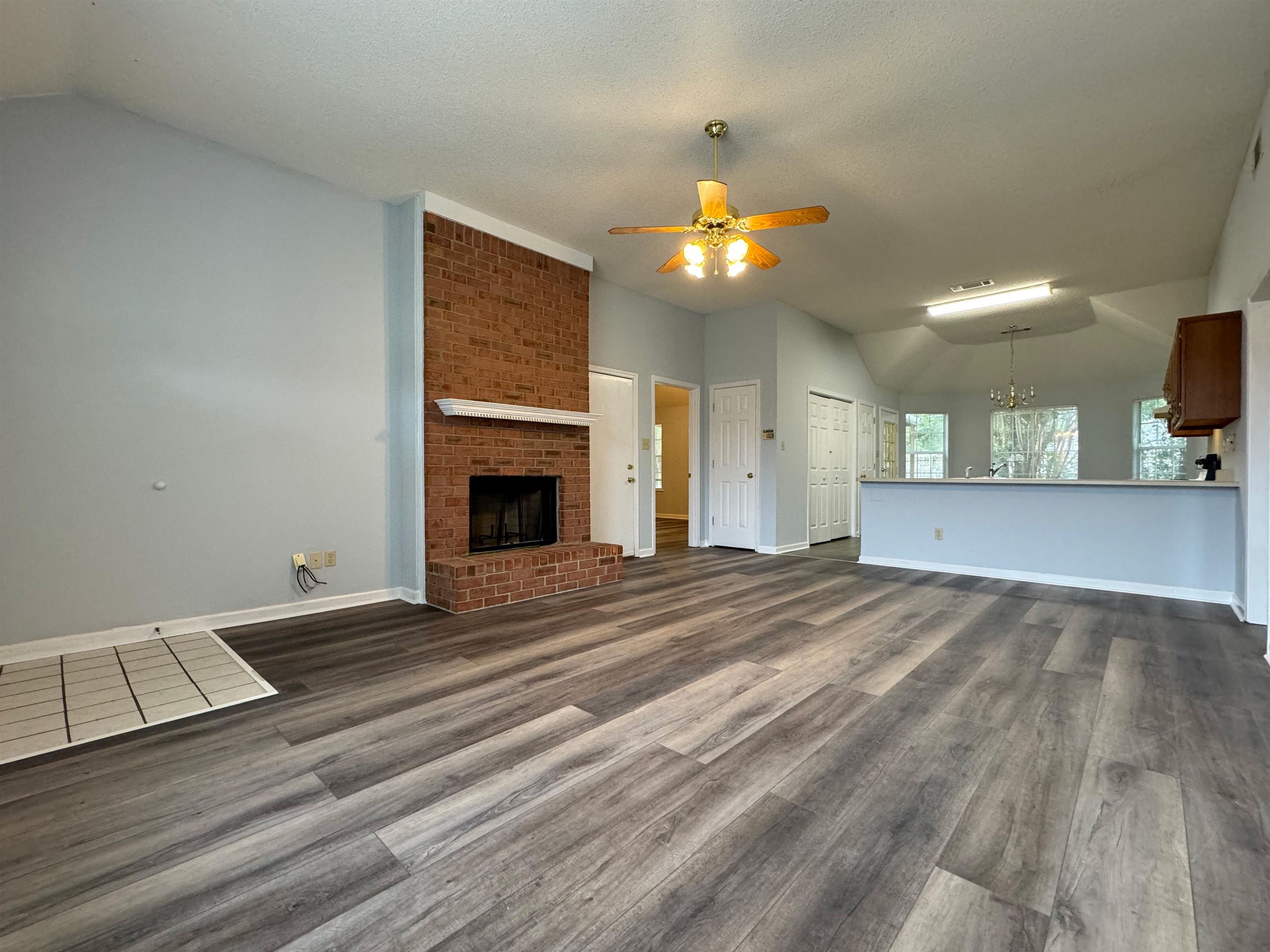 7083 Bryan Station Road Cordova, TN 38018 - Photo 5 of 19 Unfurnished living room featuring ceiling fan with notable chandelier, lofted ceiling, dark wood-type flooring, and a brick fireplace