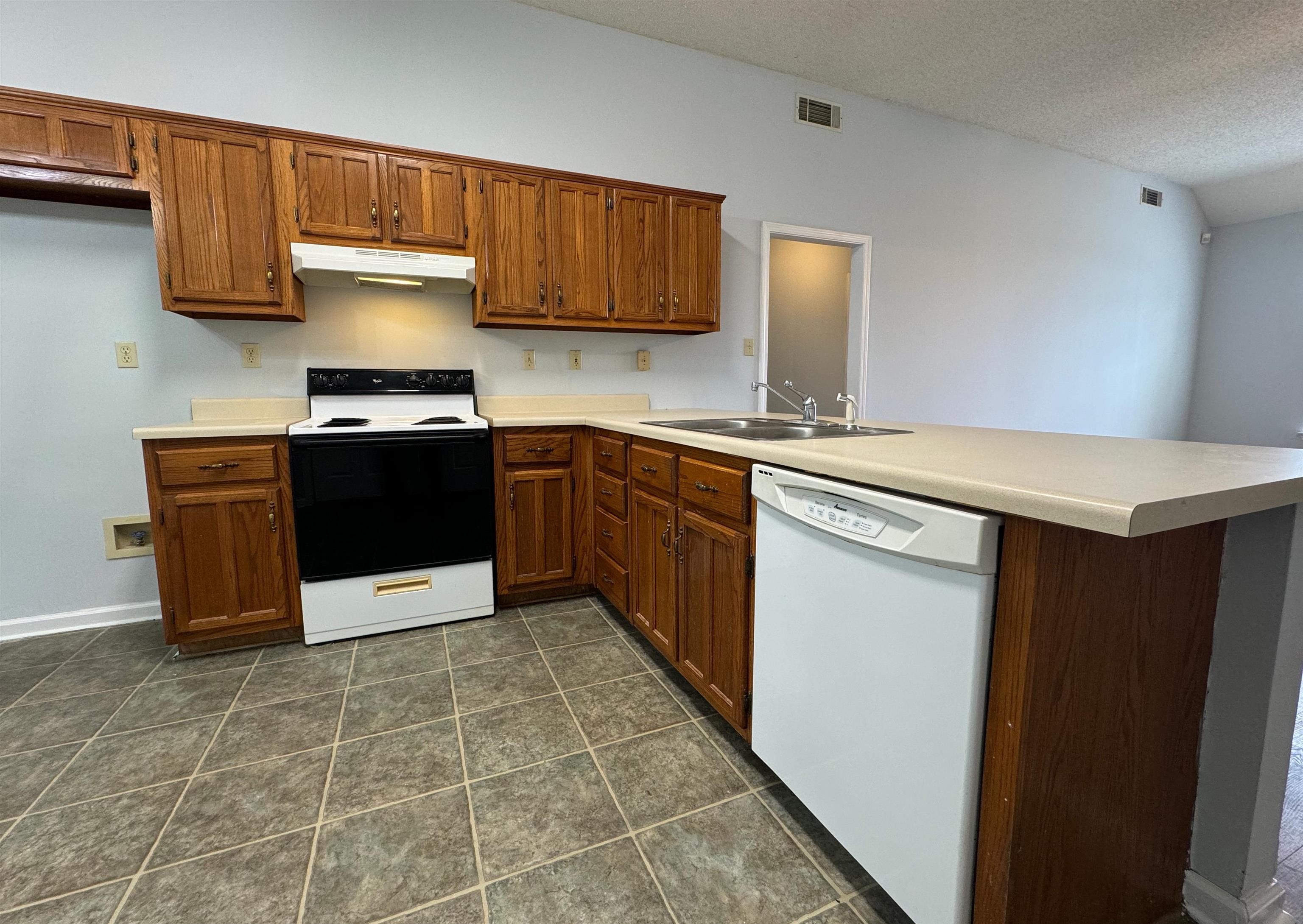 7083 Bryan Station Road Cordova, TN 38018 - Photo 8 of 19 Kitchen with dark tile patterned flooring, a textured ceiling, sink, kitchen peninsula, and white appliances
