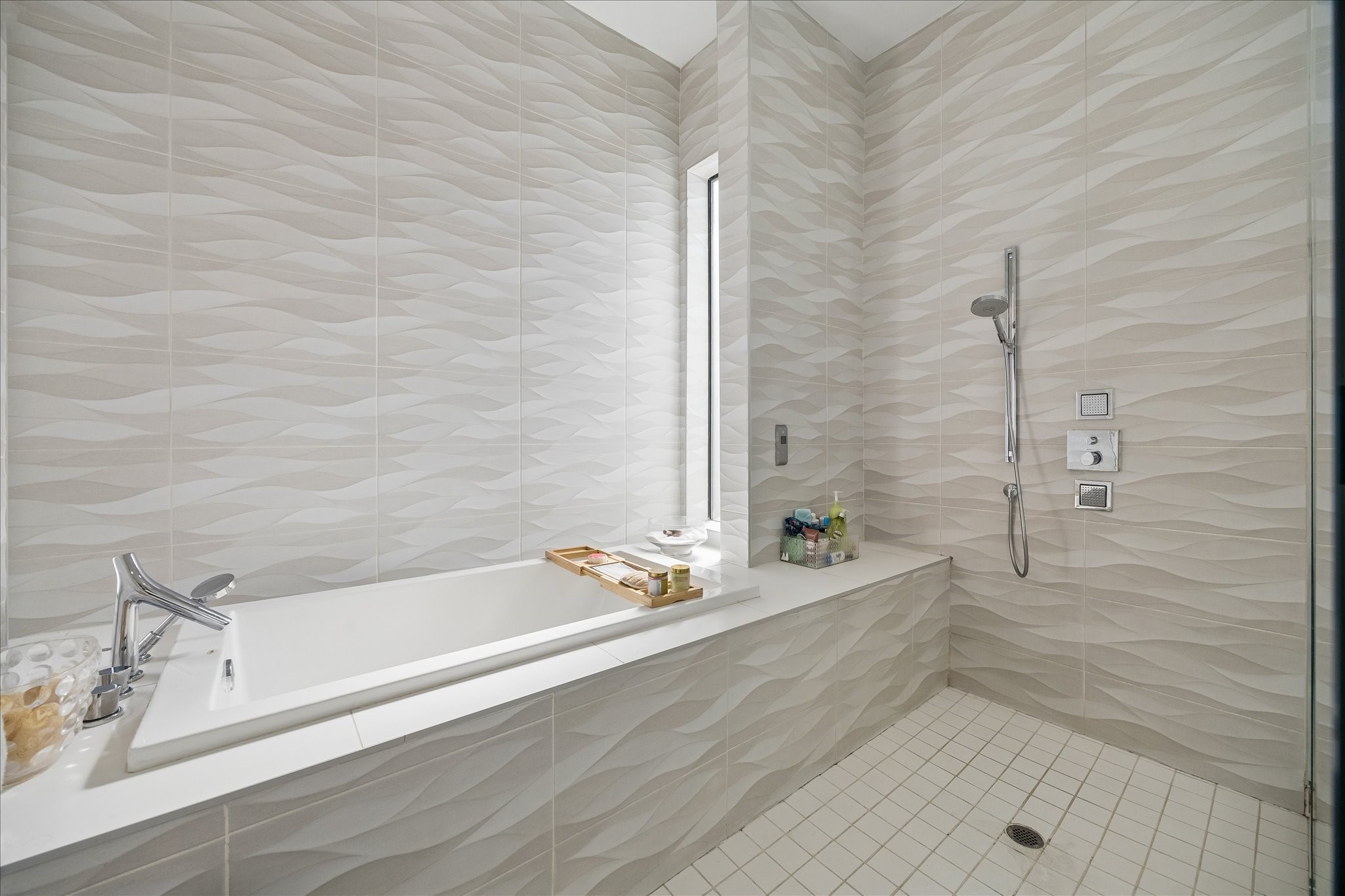 2014 Park Street Houston, TX 77019 - Photo 24 of 40 This modern bathroom features a sleek, built-in bathtub with a chrome faucet, complemented by textured wave-patterned tiles and a separate shower area with a handheld showerhead.
