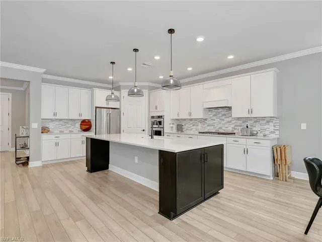 a large white kitchen with kitchen island a sink a center island and stainless steel appliances