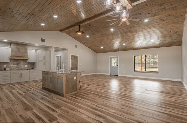 a kitchen with kitchen island granite countertop a stove a sink a refrigerator and white cabinets with wooden floor