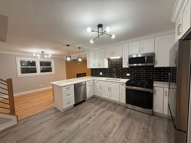 a kitchen with granite countertop a refrigerator oven a sink dishwasher and white cabinets with wooden floor