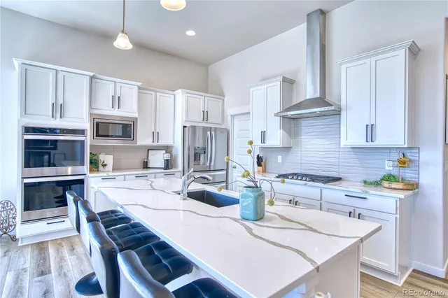 a kitchen with stainless steel appliances granite countertop a stove a sink a microwave a refrigerator a stove and white cabinets with wooden floor
