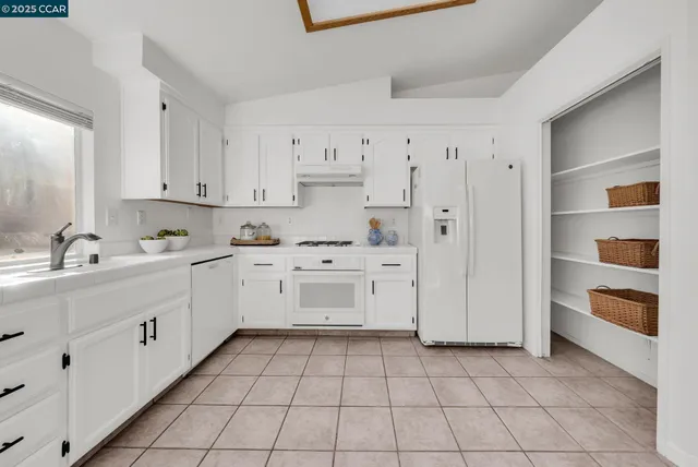 a kitchen with stainless steel appliances kitchen island granite countertop a refrigerator a stove a sink dishwasher and white cabinets with wooden floor