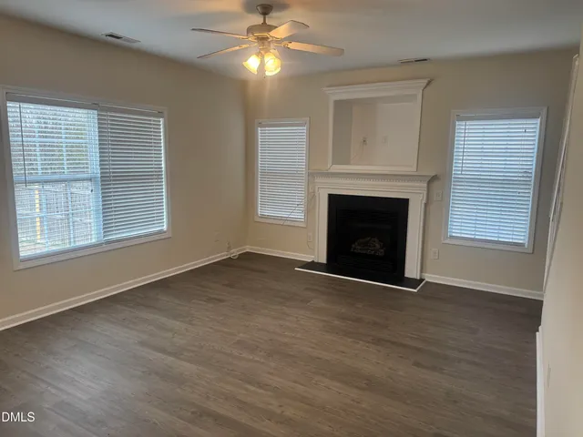 a view of an empty room with wooden floor fireplace and a window