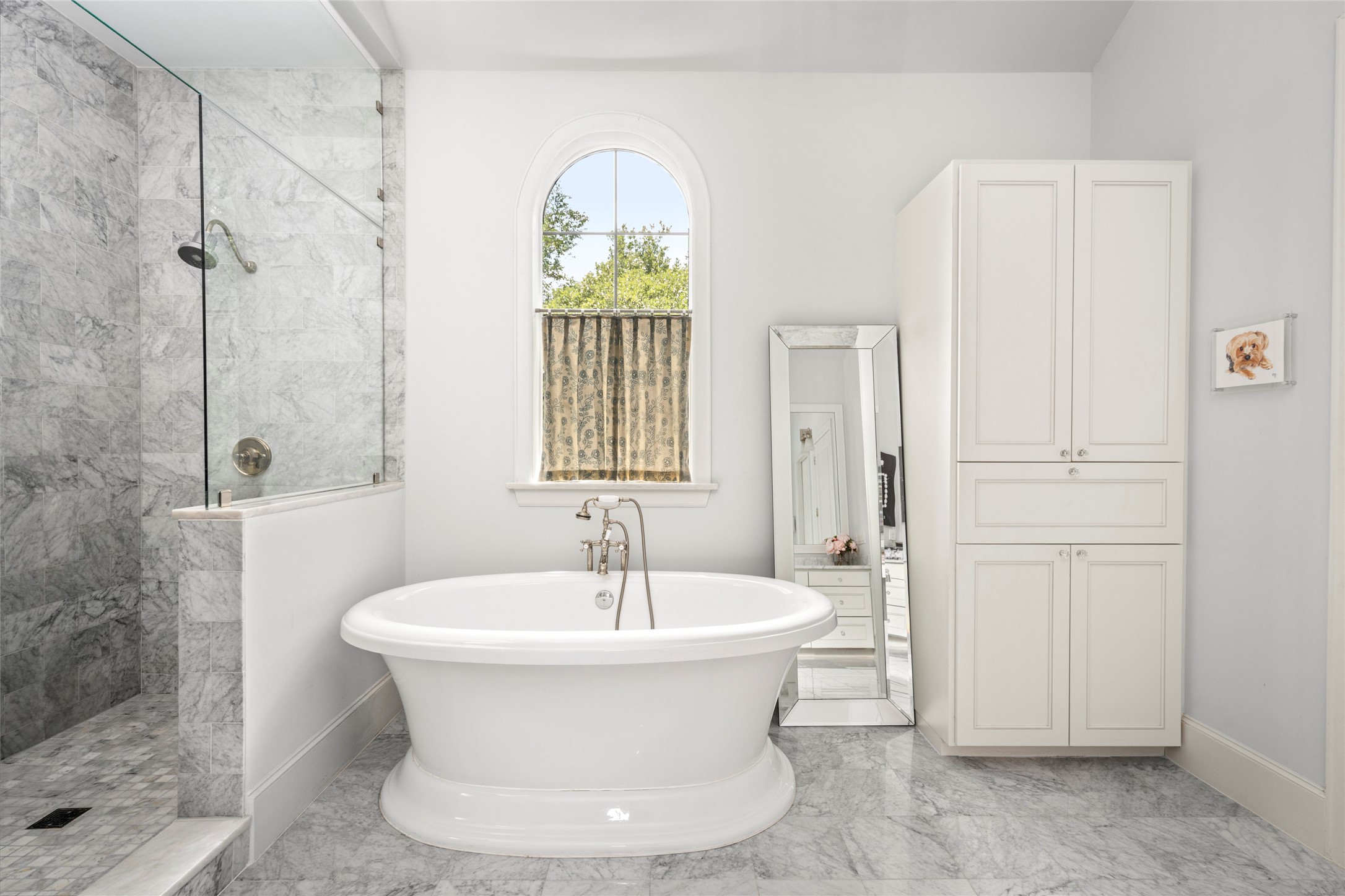 2216 Stanmore Drive Houston, TX 77019 - Photo 31 of 46 A freestanding tub is positioned beneath an arched window, with marble surfaces and built-in storage completing the tranquil bath setting.