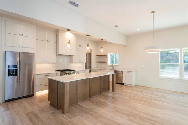 a kitchen with stainless steel appliances granite countertop a stove a sink dishwasher and a refrigerator with wooden floor