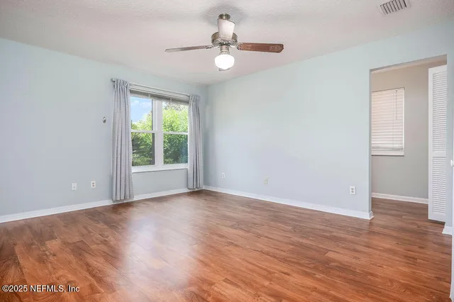 an empty room with wooden floor chandelier fan and windows