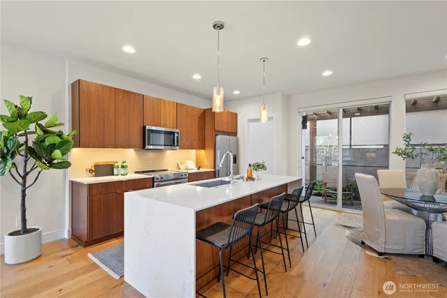 a kitchen with stainless steel appliances kitchen island granite countertop a stove a refrigerator a sink a dining table and chairs with wooden floor