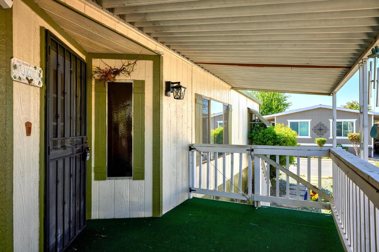 1200 South Carpenter Road, Unit 4 Modesto, CA 95351 - Photo 7 of 31 Covered front porch featuring a security screen door, wood-paneled siding, decorative green shutters, an exterior wall light, and a white baluster railing