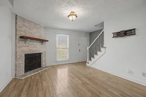 a view of an empty room with wooden floor fireplace and a window