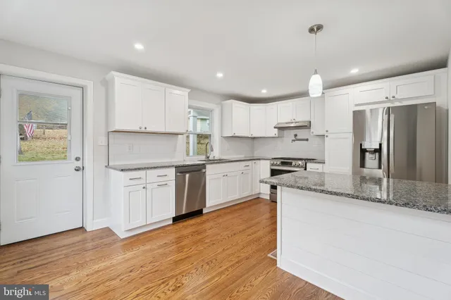 a kitchen with granite countertop a refrigerator oven a sink and white cabinets