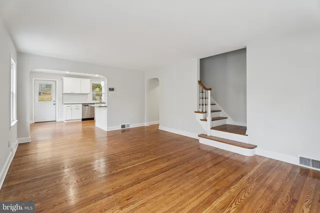 a view of empty room with wooden floor and kitchen