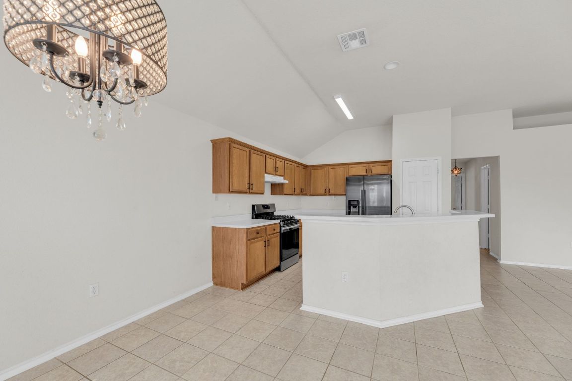 2317 Chestnut Path Round Rock, TX 78664 - Photo 11 of 36 Kitchen featuring stainless steel appliances, brown cabinets, light countertops, lofted ceiling, and light tile patterned floors