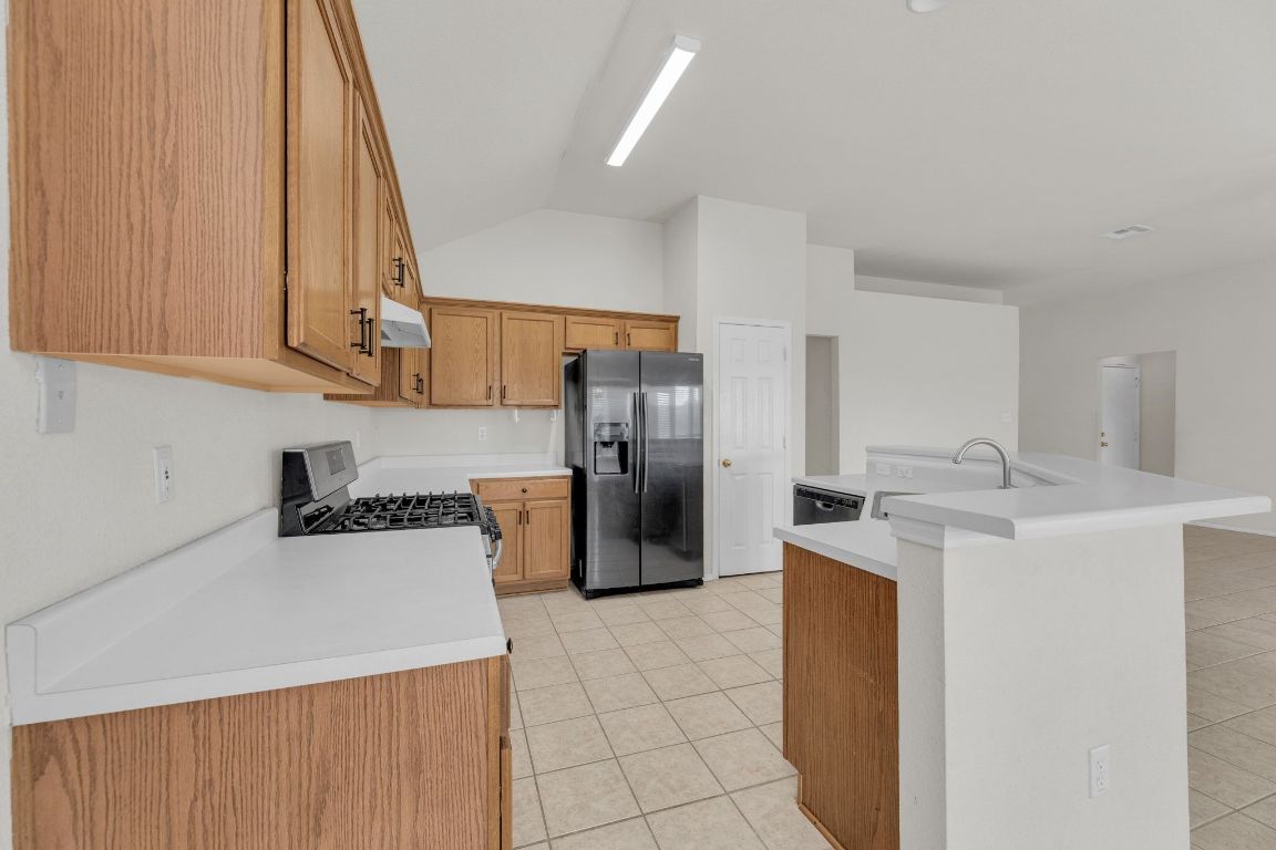 2317 Chestnut Path Round Rock, TX 78664 - Photo 13 of 36 Kitchen with light tile patterned floors, appliances with stainless steel finishes, a kitchen island with sink, light countertops, and vaulted ceiling