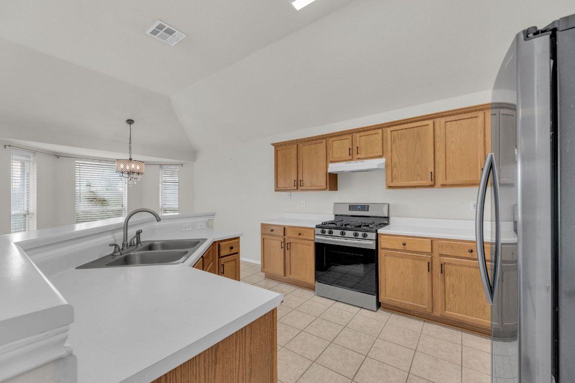 2317 Chestnut Path Round Rock, TX 78664 - Photo 14 of 36 Kitchen featuring appliances with stainless steel finishes, lofted ceiling, light countertops, under cabinet range hood, and light tile patterned floors
