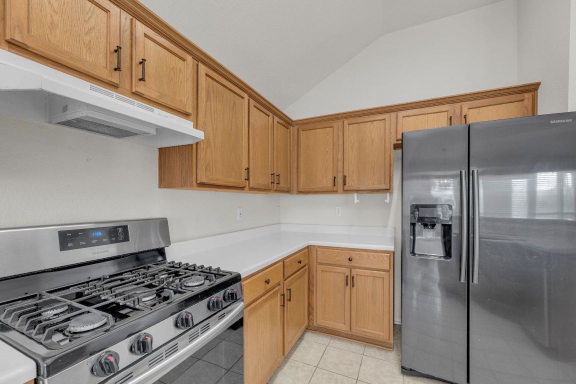 2317 Chestnut Path Round Rock, TX 78664 - Photo 16 of 36 Kitchen with stainless steel appliances, light countertops, vaulted ceiling, under cabinet range hood, and light tile patterned floors