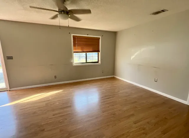 an empty room with wooden floor fan and windows