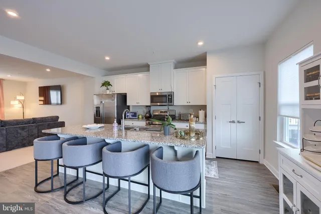 a kitchen with stainless steel appliances kitchen island granite countertop a dining table chairs and a refrigerator