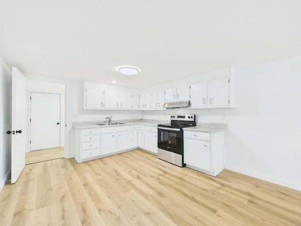 a large white kitchen with granite countertop a sink white cabinets and stainless steel appliances