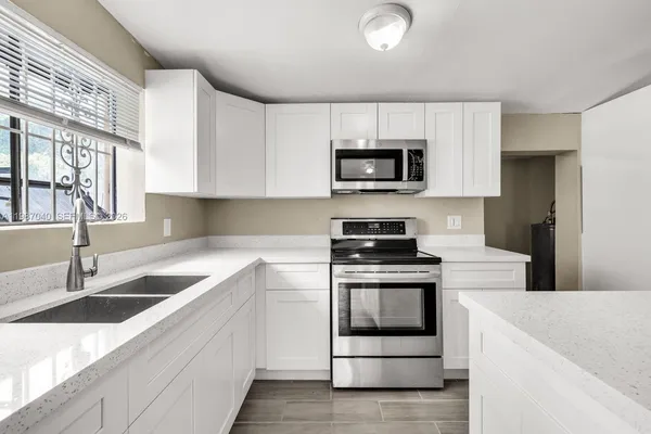 a kitchen with stainless steel appliances granite countertop white cabinets a sink a stove and a microwave