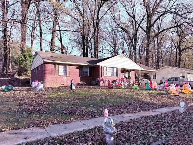 a front view of a house with yard and covered with trees