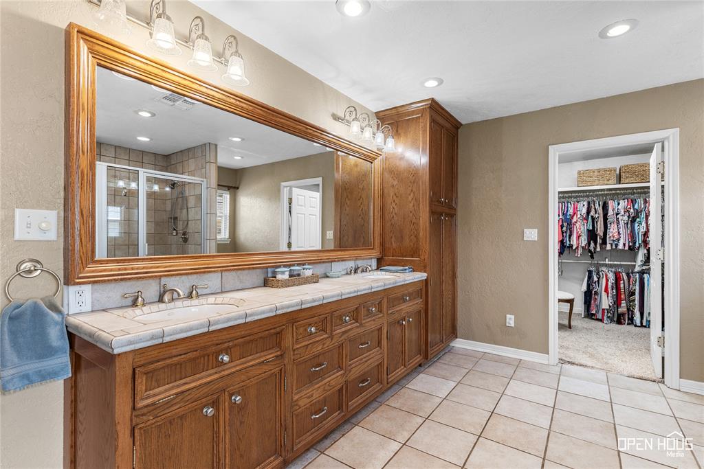 3316 Kessler Boulevard Wichita Falls, TX 76309 - Photo 21 of 35 Bathroom featuring an extended wood-finish vanity with dual sinks, tiled countertop, and a large framed mirror