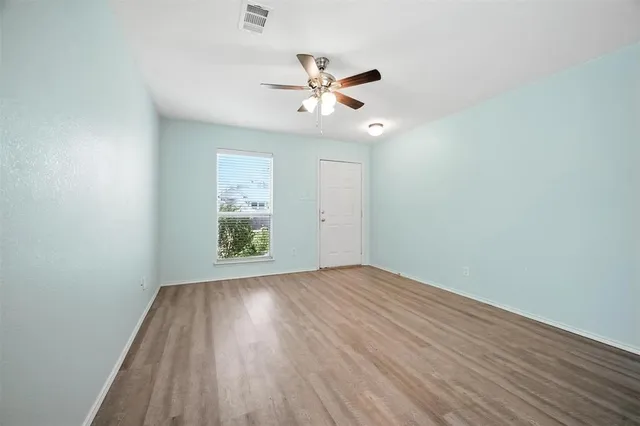 an empty room with wooden floor window and ceiling fan