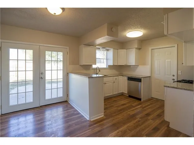 a kitchen with stainless steel appliances granite countertop a stove a sink dishwasher and white cabinets with wooden floor