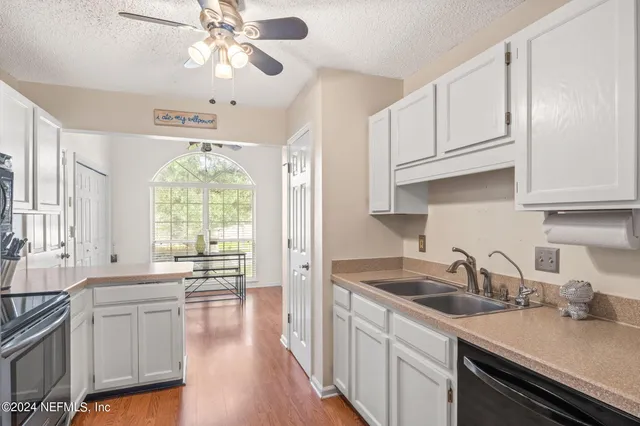 a kitchen with a sink dishwasher a stove and white cabinets with wooden floor