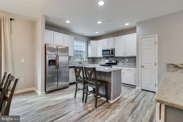 a kitchen with kitchen island granite countertop a refrigerator stove a sink and white cabinets with wooden floor