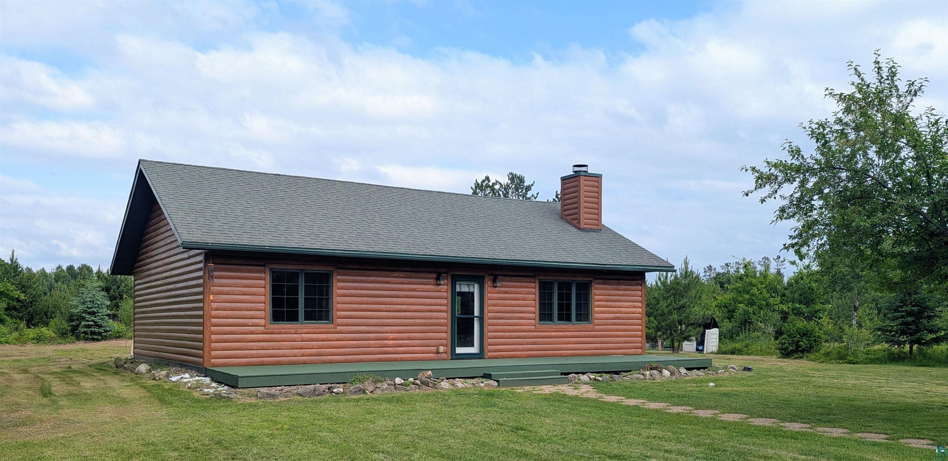 86196 Military Road Sturgeon Lake, MN 55783 - Photo 3 of 4 Log-sided residence featuring a dark shingle roof, a prominent chimney, and a full-length front deck