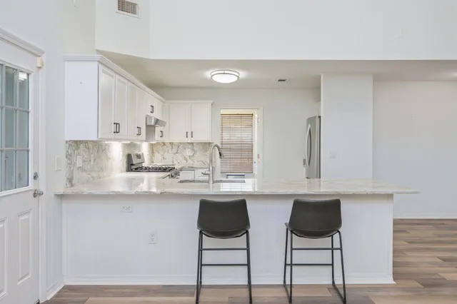 a kitchen with stainless steel appliances granite countertop a stove a sink and white cabinets with wooden floor