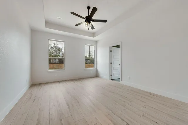 an empty room with wooden floor ceiling fan and windows