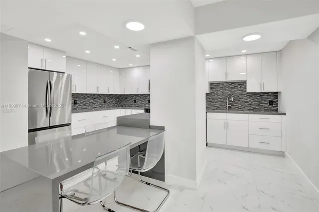 a kitchen with stainless steel appliances kitchen island granite countertop a refrigerator sink and white cabinets