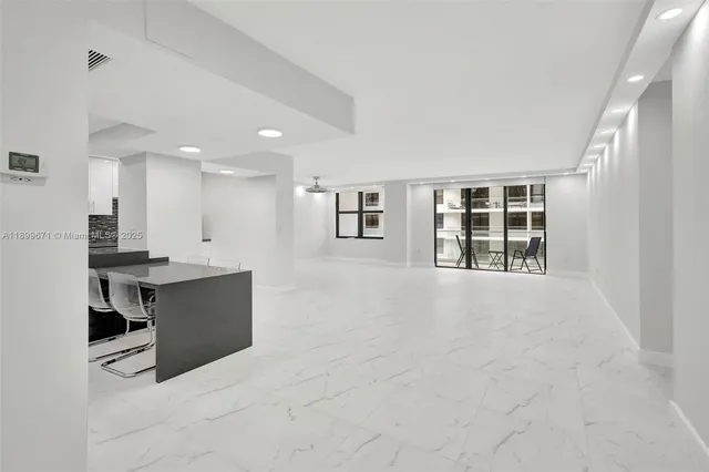 a view of an empty room with kitchen and window