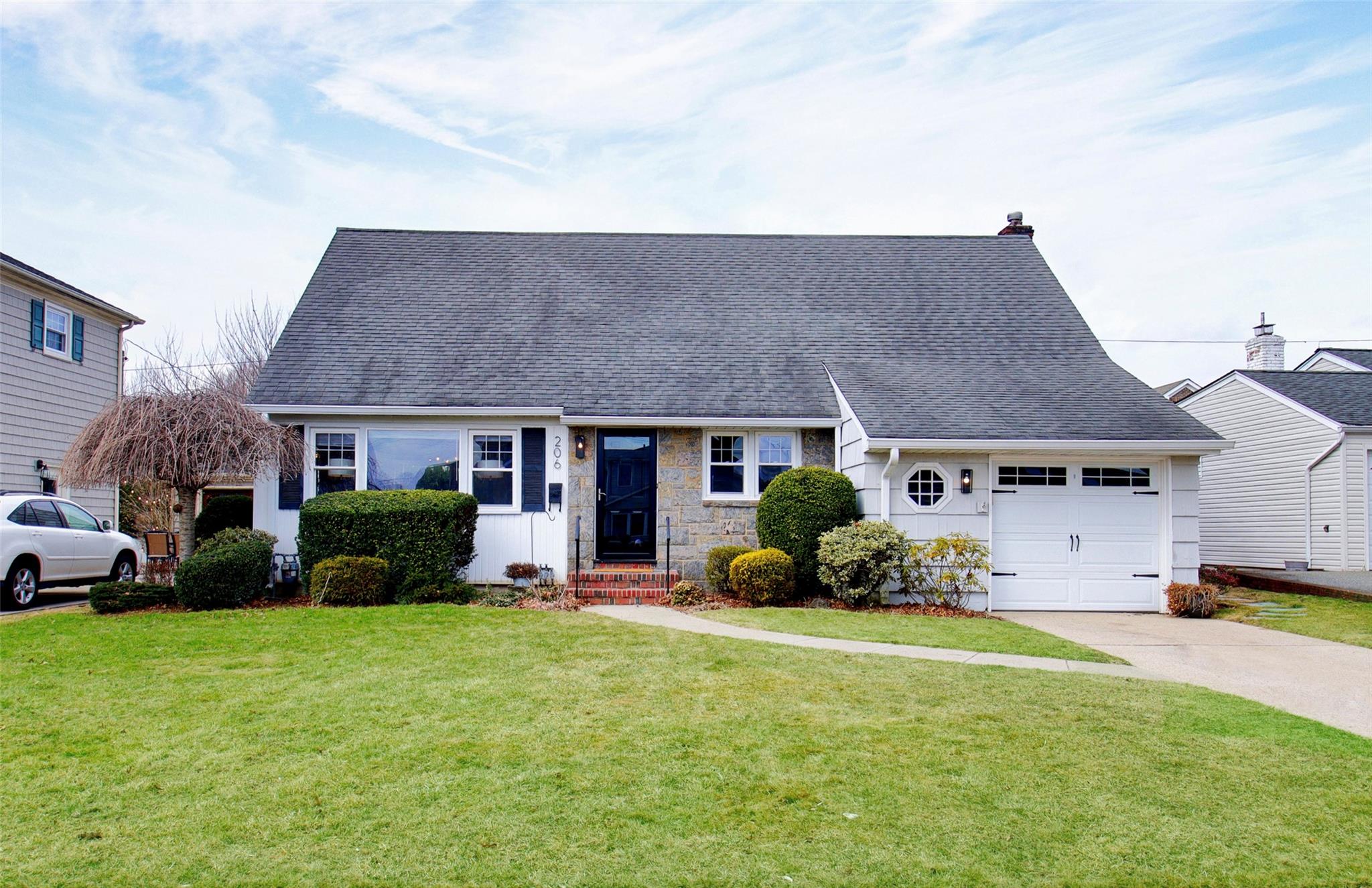 View of front of home with a shingled roof, concrete driveway, a garage, stone siding, and a front lawn