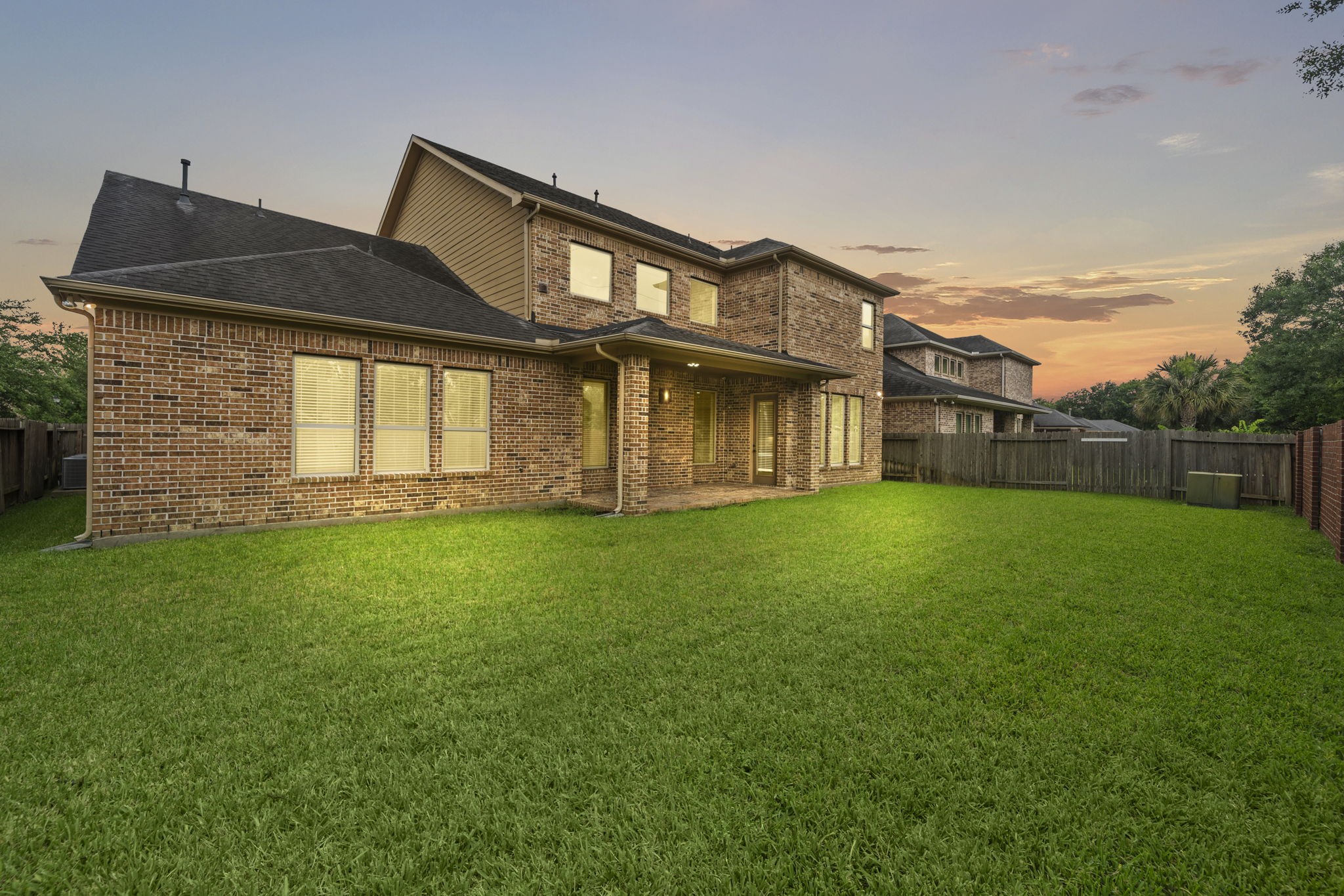 14215 Spindle Arbor Road Cypress, TX 77429 - Photo 7 of 47 This photo showcases a spacious backyard with a well-maintained lawn and a two-story brick house at sunset. The home features large windows and a covered patio, ideal for outdoor relaxation.