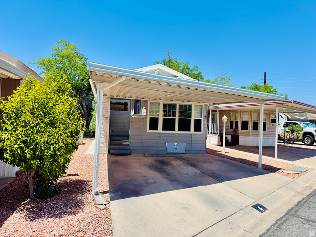 150 North 3050 East, Unit 4 St. George, UT 84790 - Photo 2 of 24 Exterior featuring a covered carport, light gray siding, multi-pane windows, elevated entry steps, and a decorative landscape with a mature shrub and red stone ground cover