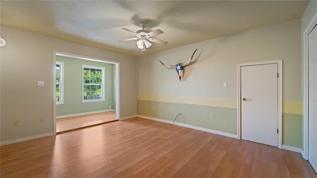 an empty room with wooden floor chandelier fan and windows