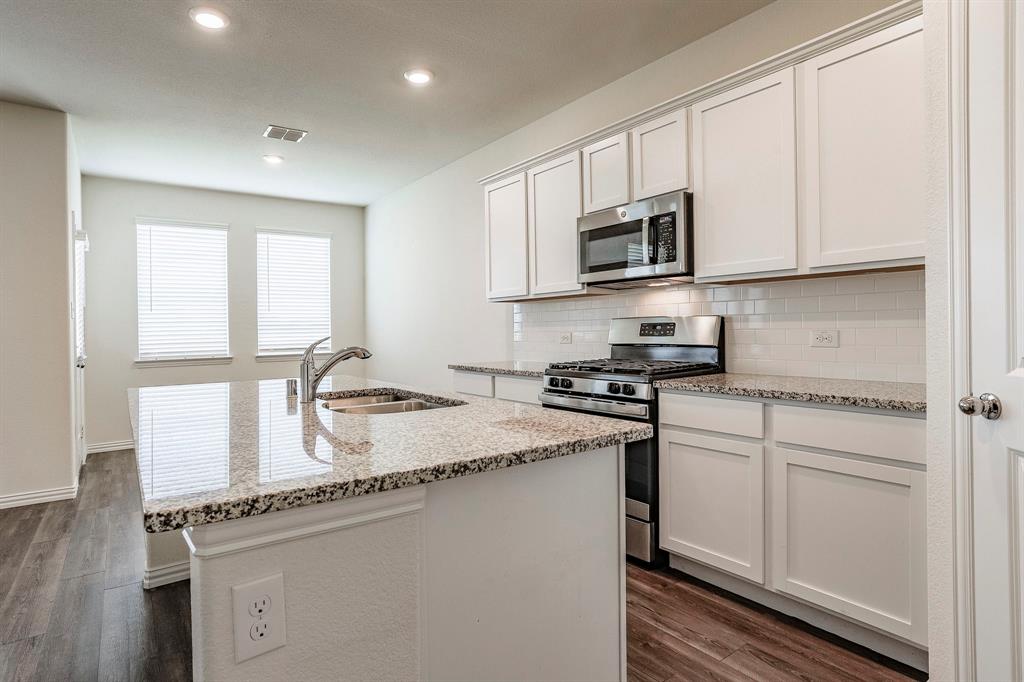 652 Ridgeback Trail Fort Worth, TX 76052 - Photo 10 of 20 Kitchen featuring sink, appliances with stainless steel finishes, dark hardwood / wood-style floors, white cabinets, and a center island with sink