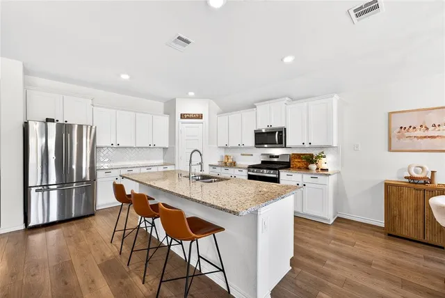 a kitchen with stainless steel appliances granite countertop a refrigerator a stove a sink a dining table and chairs with wooden floor