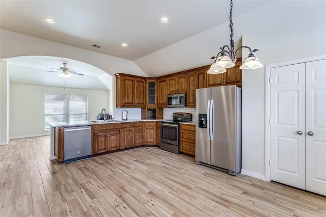 a kitchen with stainless steel appliances kitchen island granite countertop a refrigerator a sink dishwasher a stove and a dining table with wooden floor